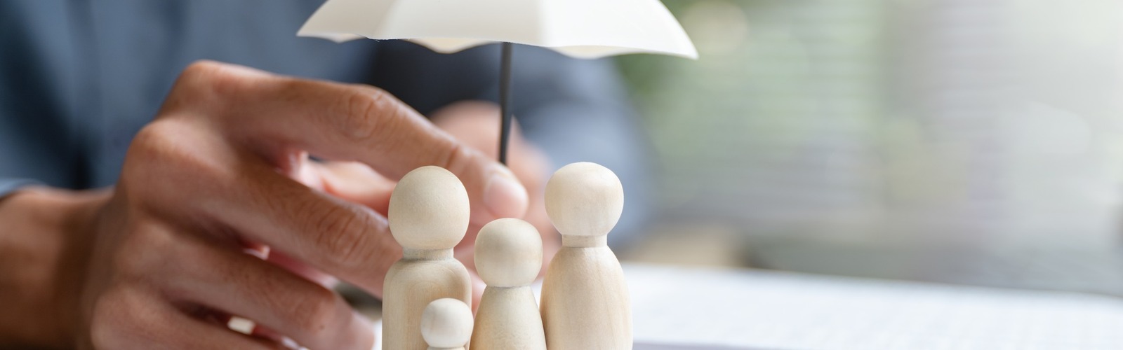 Holzfiguren symbolisieren eine Familie, geschützt durch einen Regenschirm