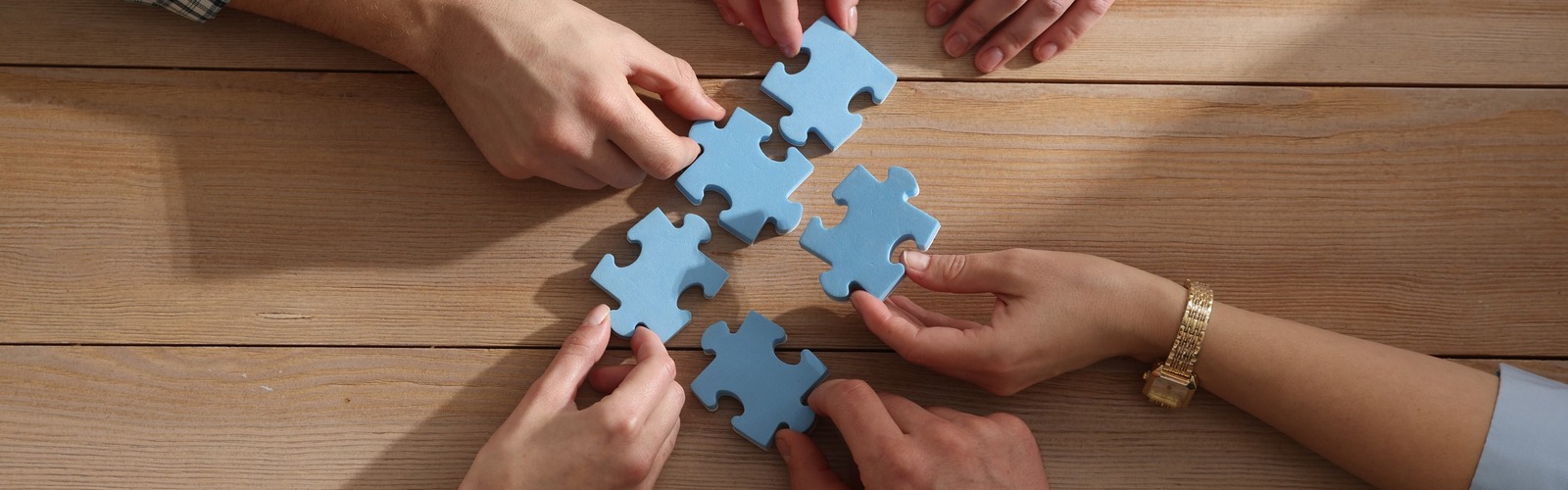 Hände halten einzelne Puzzleteile, die zusammenpassen