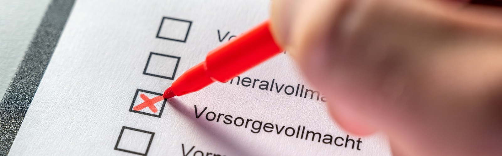 Jemand setzt ein Kreuz auf einem Papier, neben Vorsorgevollmacht